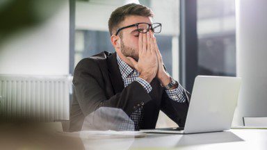 Frustrated man rubbing eyes in front of laptop because he has to read another article about the Great Resignation.
